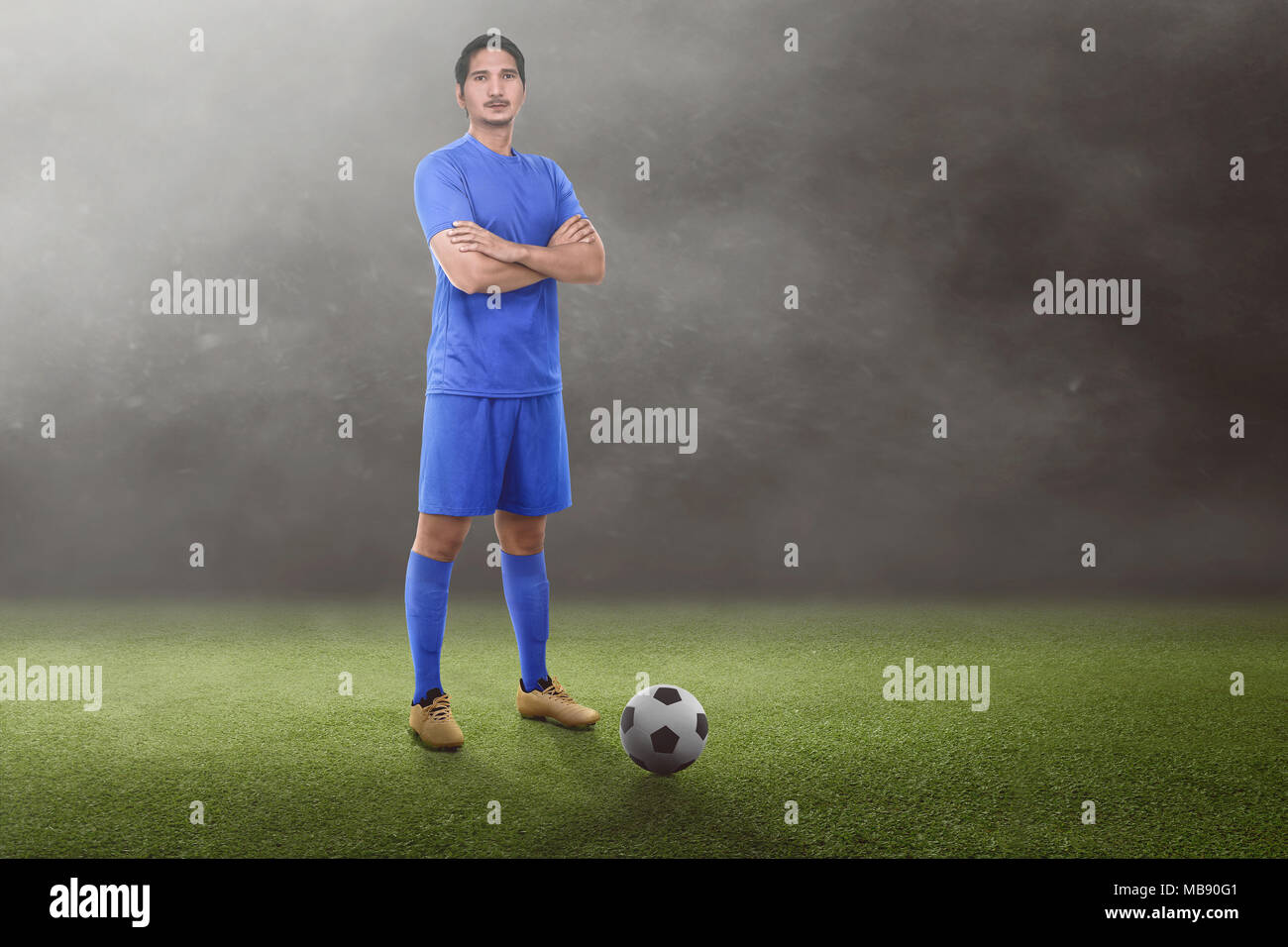 Bello asian giocatore di football con bracci incrociati sul campo in erba Foto Stock