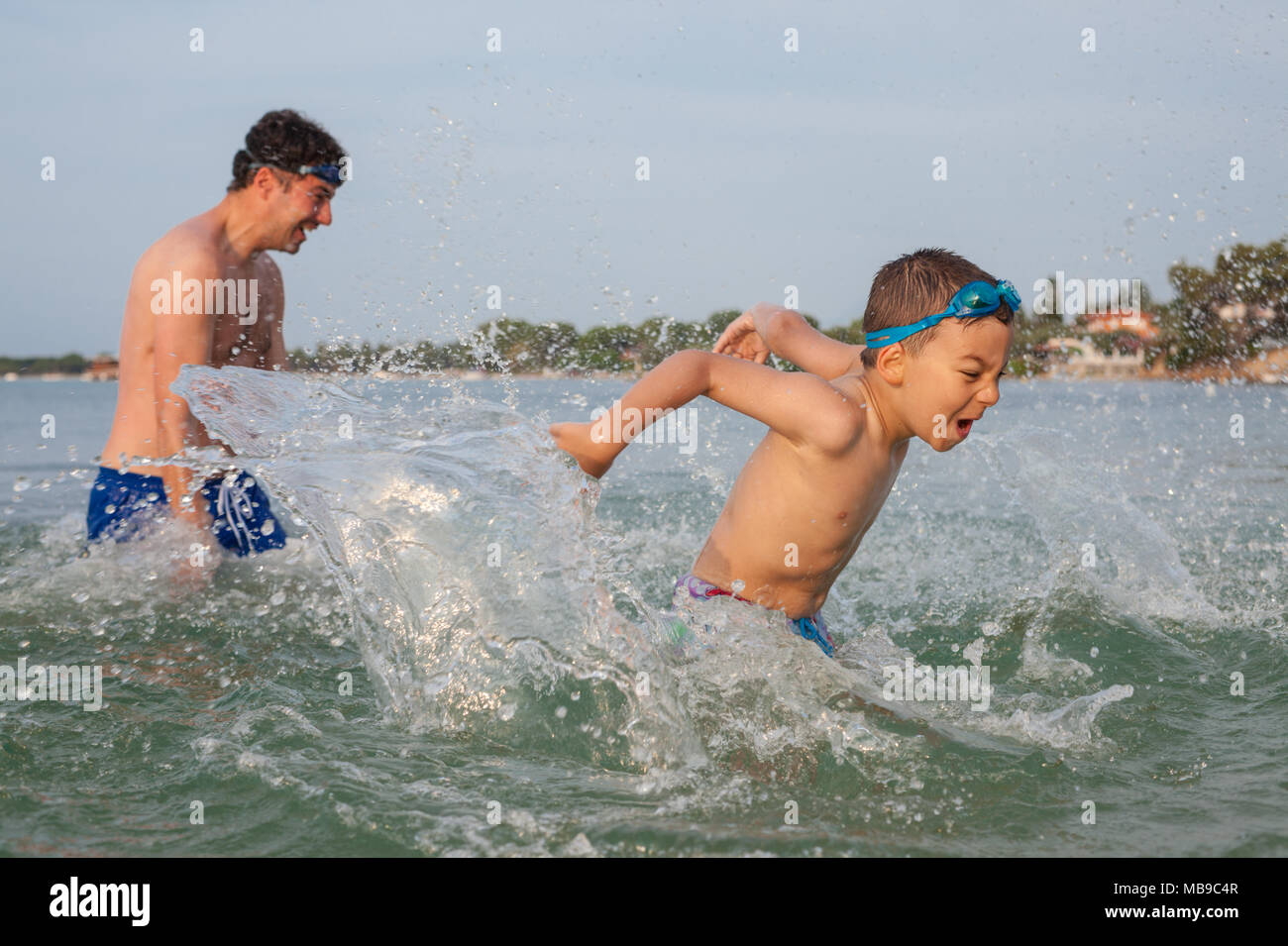 Ragazzo figlio Padre gioco di spruzzi di mare Foto Stock