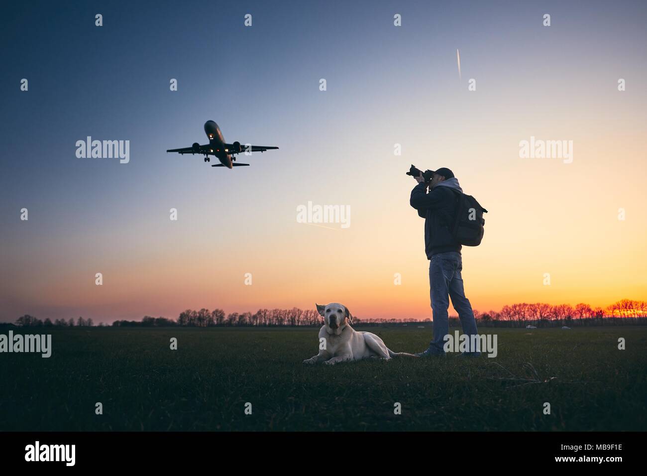 Giovane con cane è fotografare vicino aeroporto. Atterraggio aereo aginst moody sky Cielo di tramonto dorato. Foto Stock