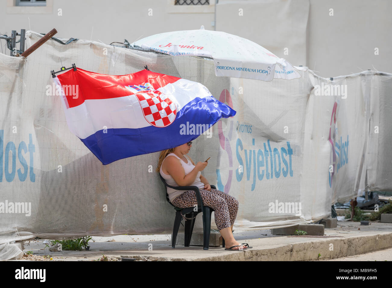 Donna con uno smart phone seduto in ombra di bandiera croata di Zadar Foto Stock