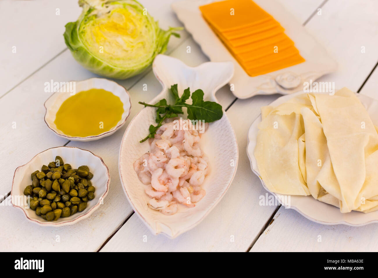 Ingredienti per la pasta sfoglia con gamberetti, olio d'oliva, sottile flatbread fogli, capperi e formaggio bianco sul tavolo in legno Foto Stock