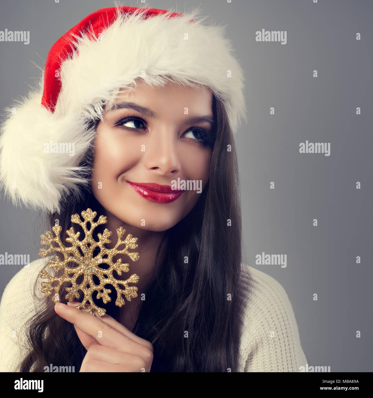 Bella Donna di natale in santa Hat Holding Golden Fiocco di neve e guardando verso l'alto. Modello di moda con il trucco e sano lunghi capelli ricci Foto Stock