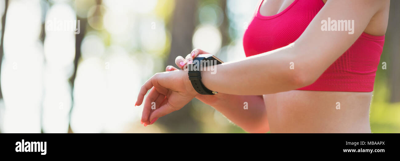 Attraente atleta femminile utilizzando app fitness sul suo orologio intelligente per monitorare le prestazioni di allenamento. Banner Web. Foto Stock