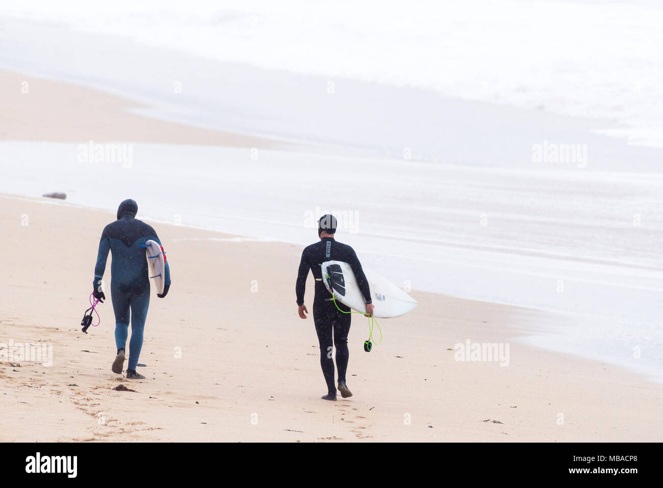 Surfers che trasportano i loro surboards come essi passeggiata a mare a Fistral Beach in Newquay Cornwall. Foto Stock