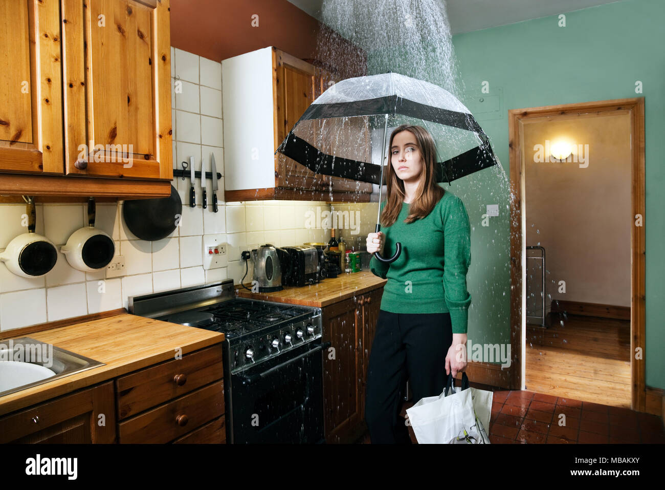 Donna in piedi in cucina con ombrello sotto la doccia di pioggia, in interni Foto Stock