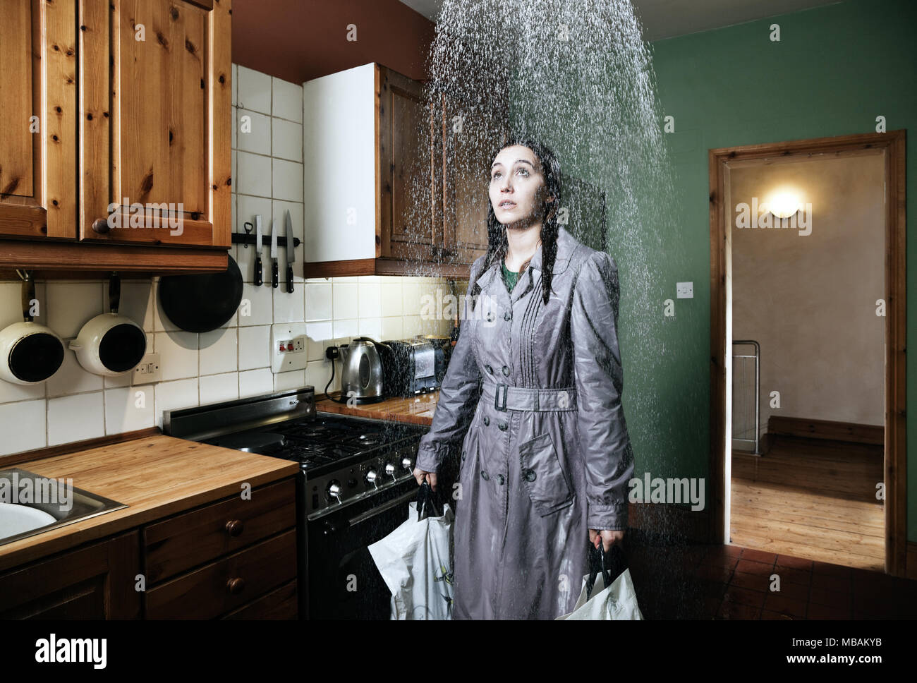 Donna in piedi in cucina sotto la doccia di pioggia, in interni Foto Stock