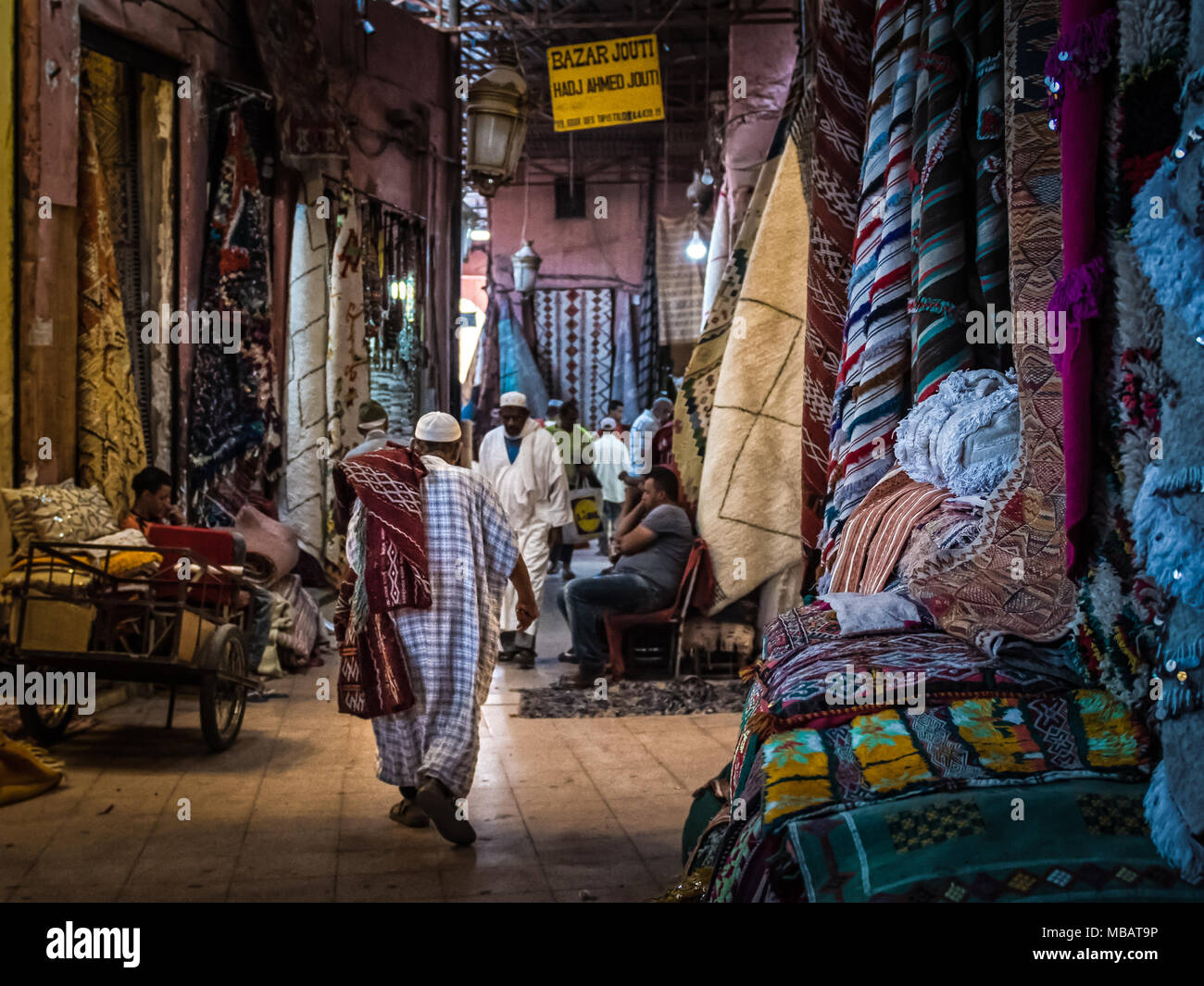 Numerosi tappeti colorati appesi al soffitto in Marrakech mercato tappeti in Marocco. Gli uomini marocchini a piedi, sit & stand nel mercato. Foto Stock