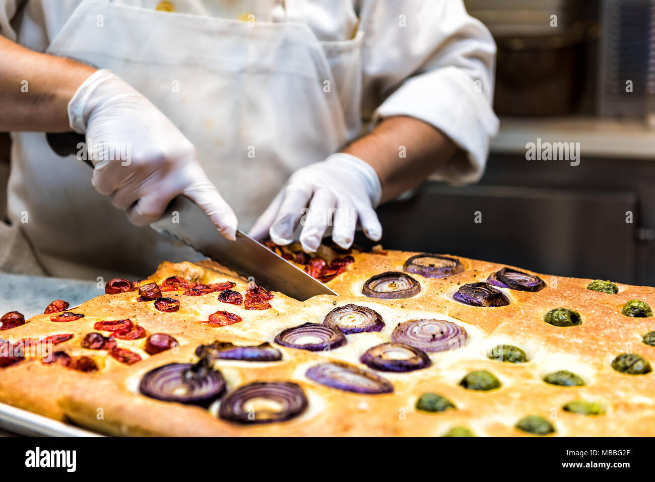 Il taglio foccacia pane con coltello, condimenti cotto in forno, lo chef del ristorante cucina con igiene sanitaria guanti Foto Stock