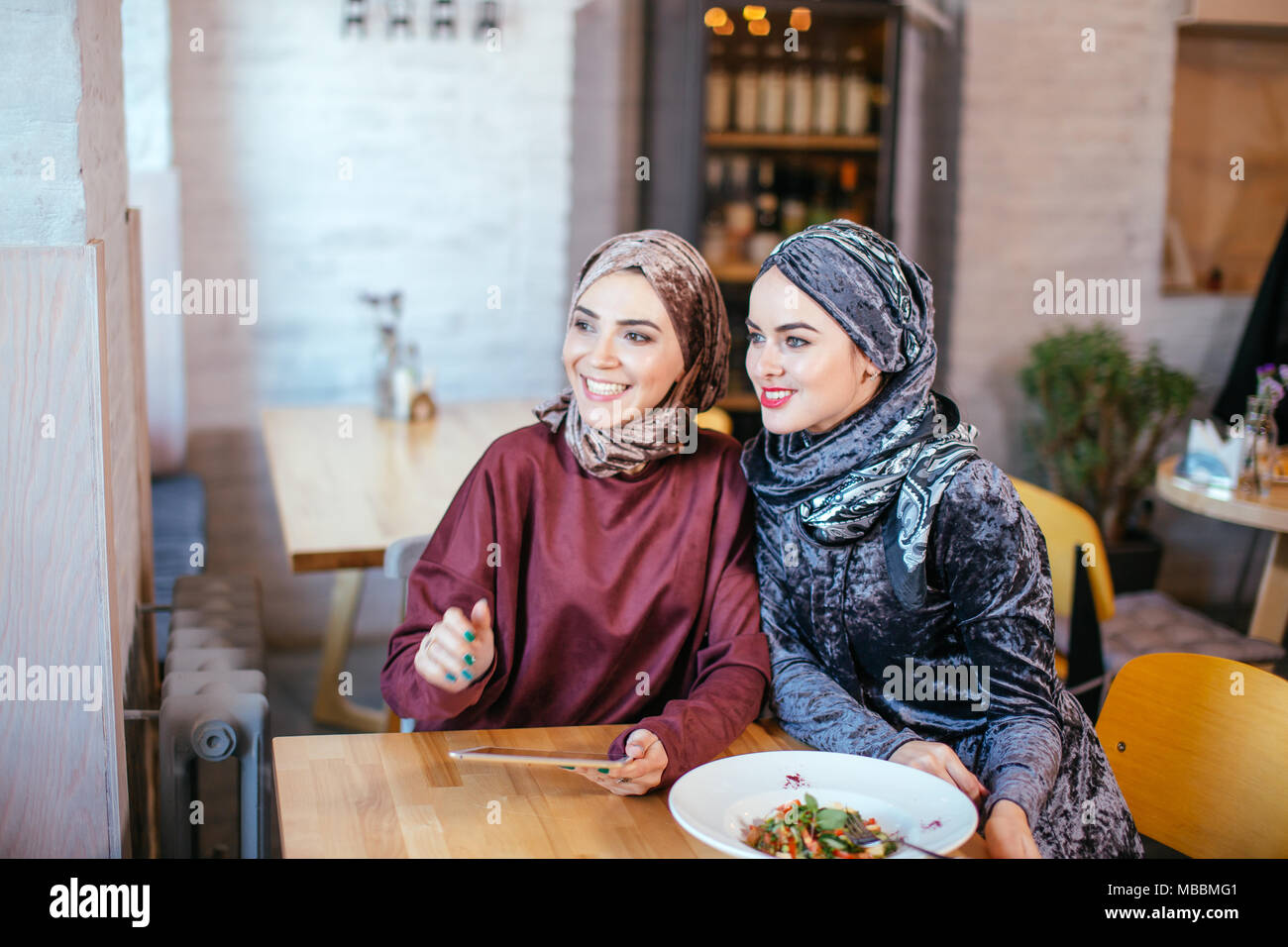 Due donne musulmane in cafe, shop online utilizzando la tavoletta elettronica Foto Stock