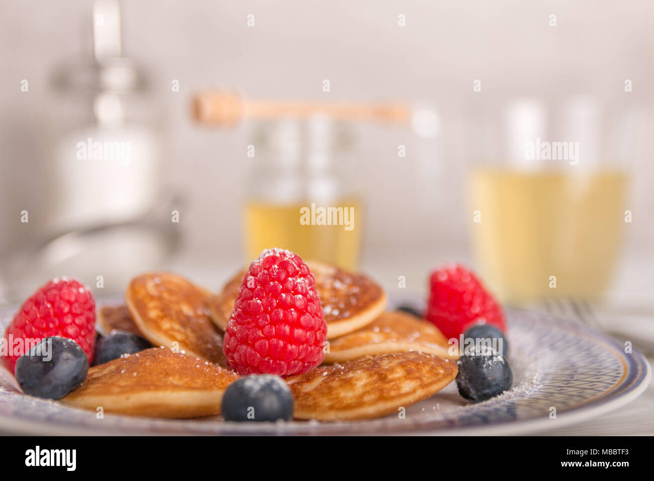 Mini pancake con frutta e miele su una piastra con tè e miele in background Foto Stock