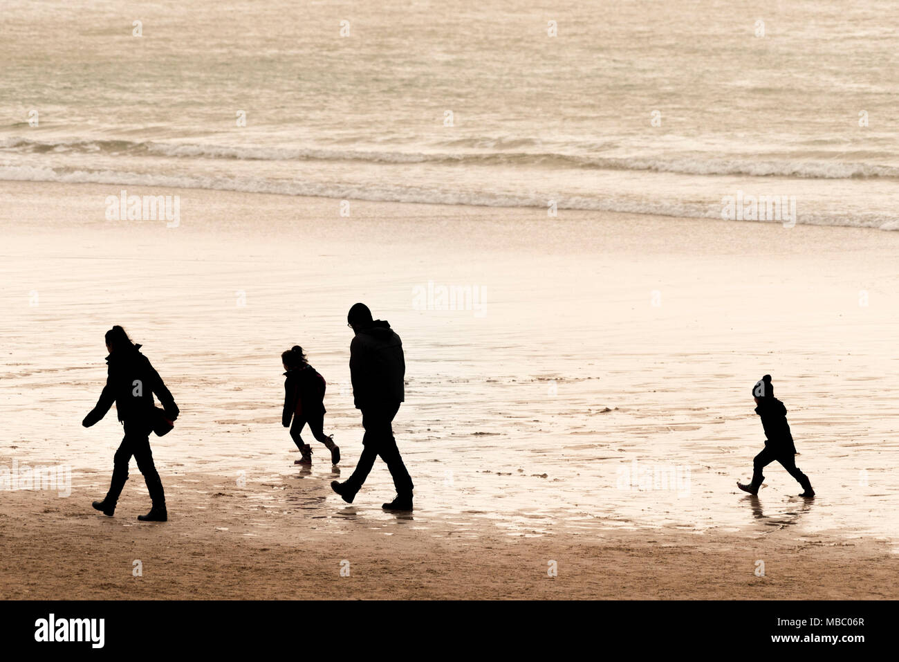 Una famiglia visto in silhouette camminando lungo una spiaggia. Foto Stock