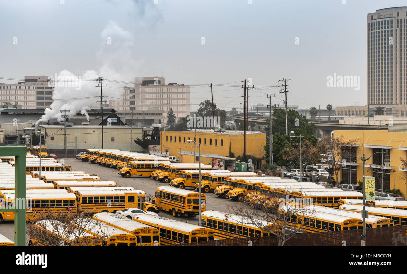 Los Angeles, CA, Stati Uniti d'America - Aprile 5, 2018: parte della grande scuola parcheggio bus su un angolo di Alameda e il College strade sotto il cielo grigio. Edifici gialli un Foto Stock