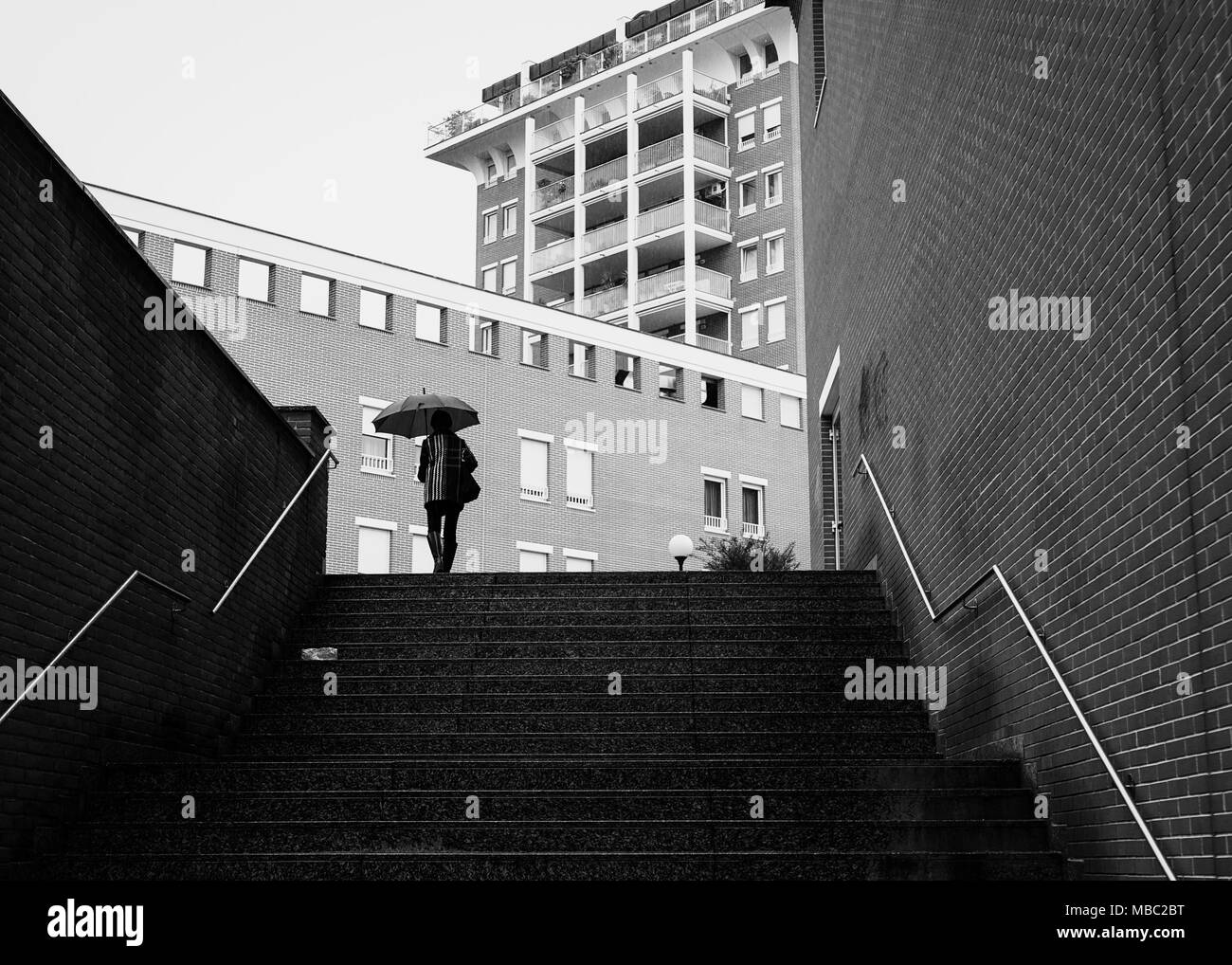 Dark paesaggistica città sotto la pioggia. Silhouette di persona sotto l'ombrello in ambiente urbano. Foto Stock