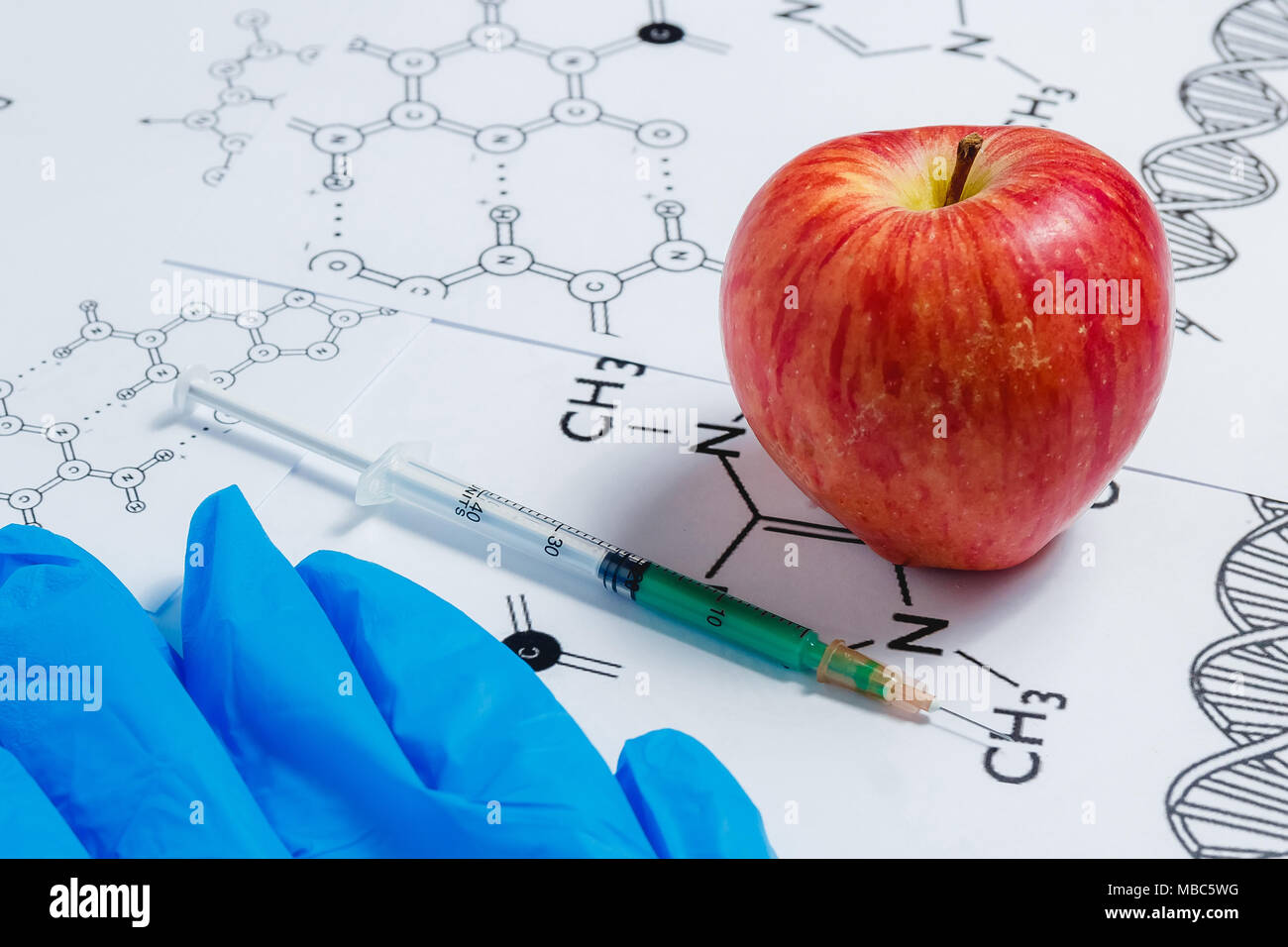 Concetto di Non-prodotti naturali, ogm. Siringa, guanti blu e rosso Apple su sfondo bianco con formula chimica Foto Stock