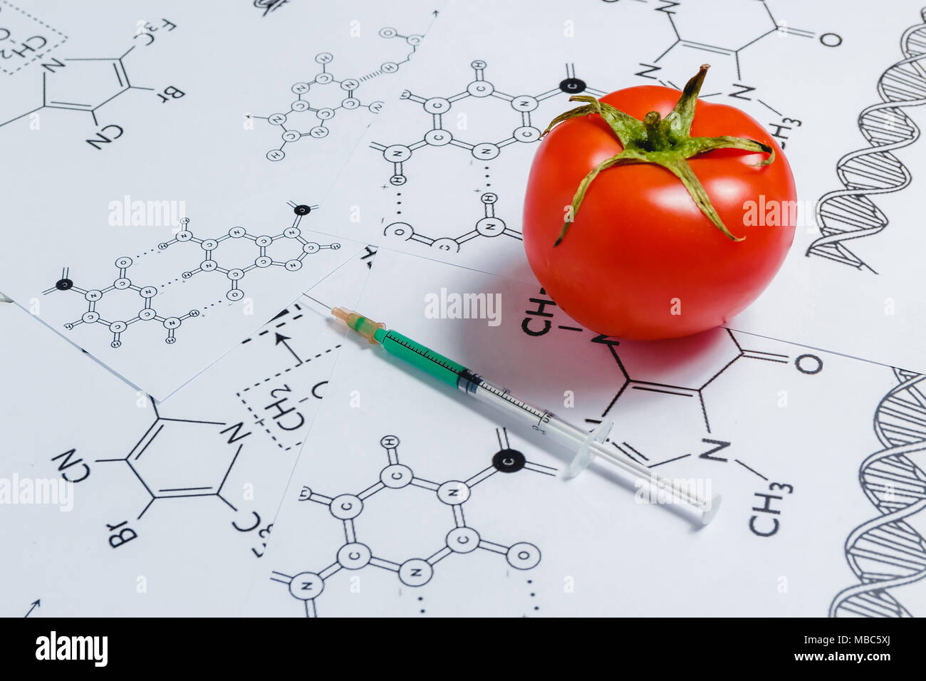 Concetto di Non-prodotti naturali, ogm. Siringa e pomodoro rosso su sfondo bianco con formula chimica Foto Stock