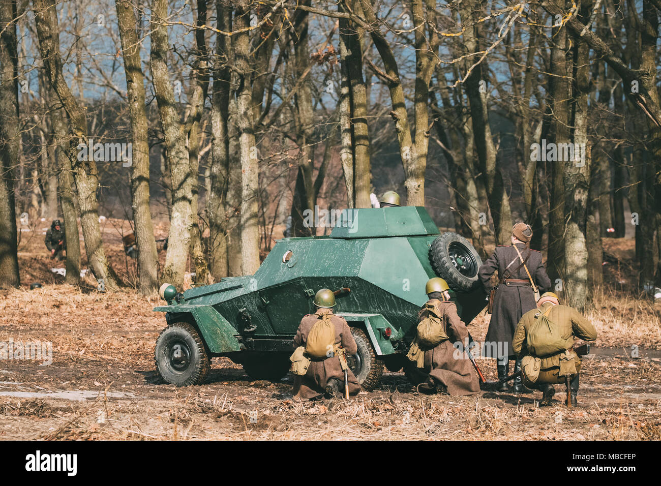 Gruppo di Reenactors vestito come Soviet russo Rosso soldati dell esercito della II Guerra Mondiale vai su offensivo sotto la copertura di corazzato sovietico auto Scout Ba-64. Histori Foto Stock