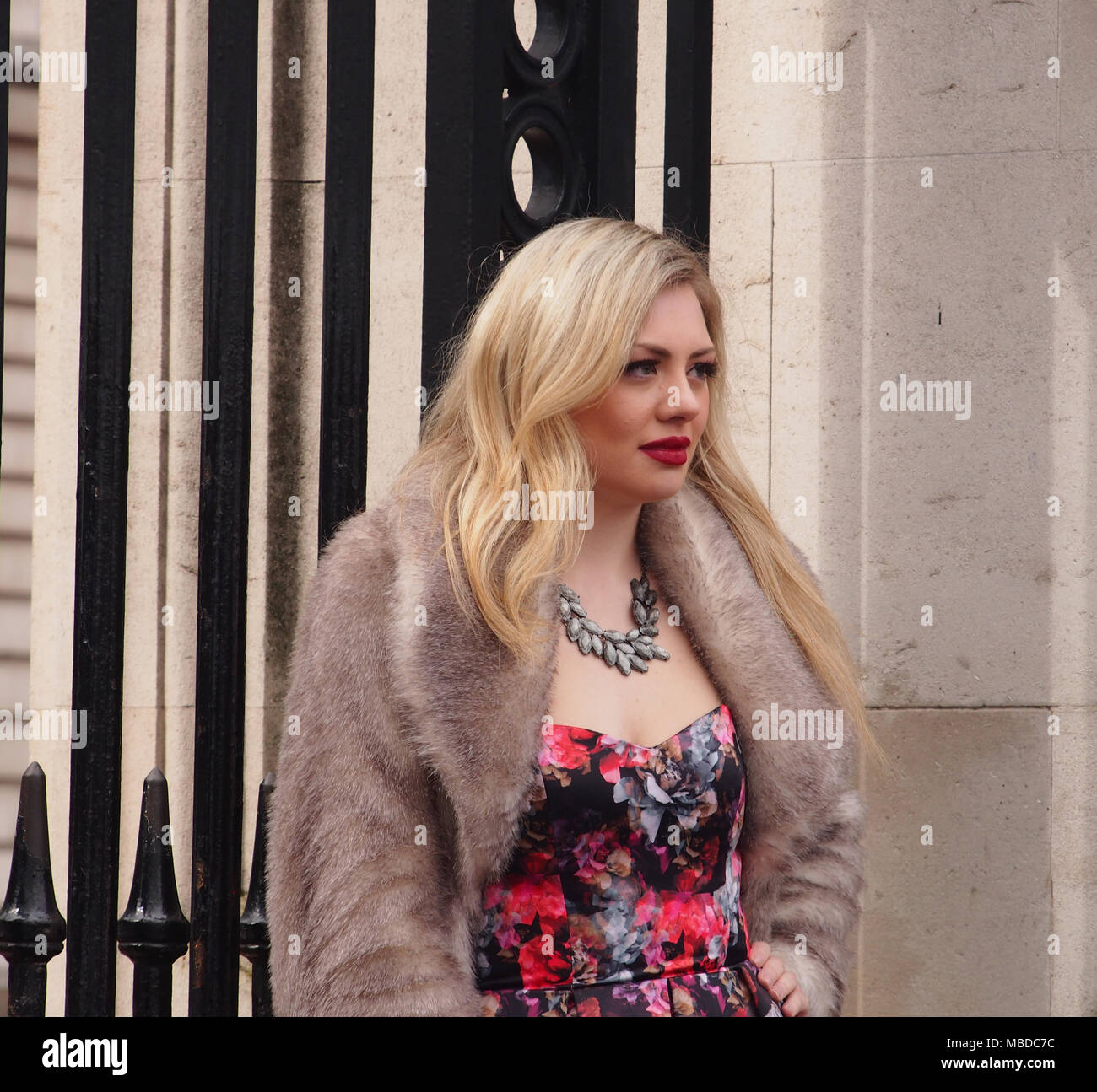 Una giovane donna con lunghi capelli biondi e fiorito di vestire in posa per una fotografia di fronte a Buckingham Palace di Londra Foto Stock