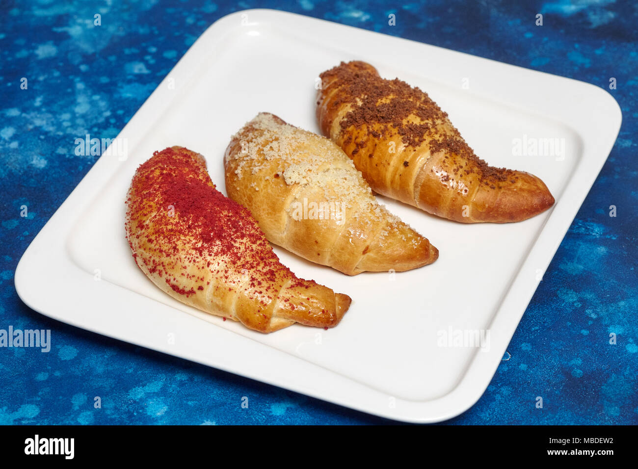 Tre freschi croissant burroso sulla piastra bianca, sfondo blu Foto Stock