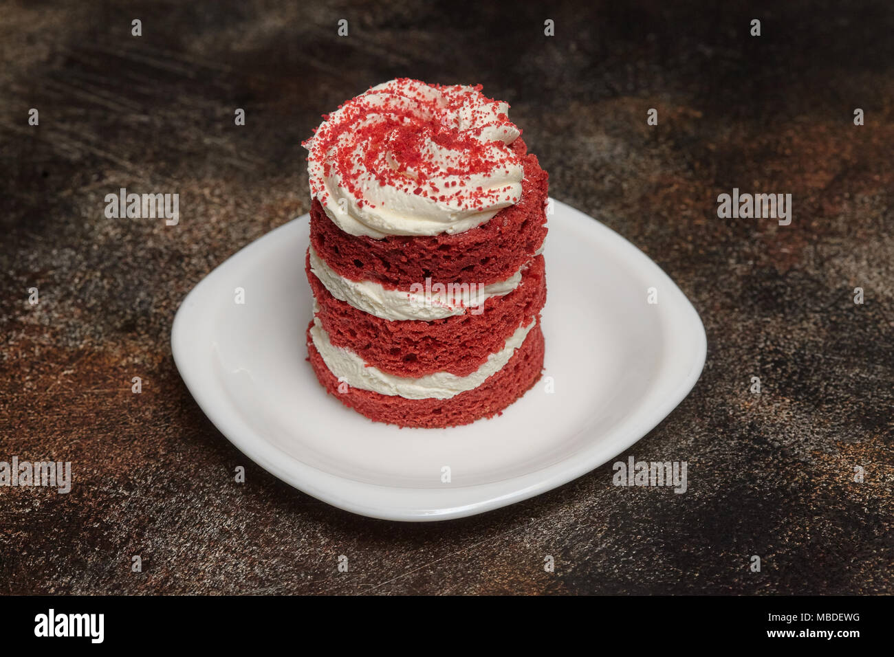 Round torta rossa del velluto con crema sulla piastra bianca, sfondo marrone Foto Stock