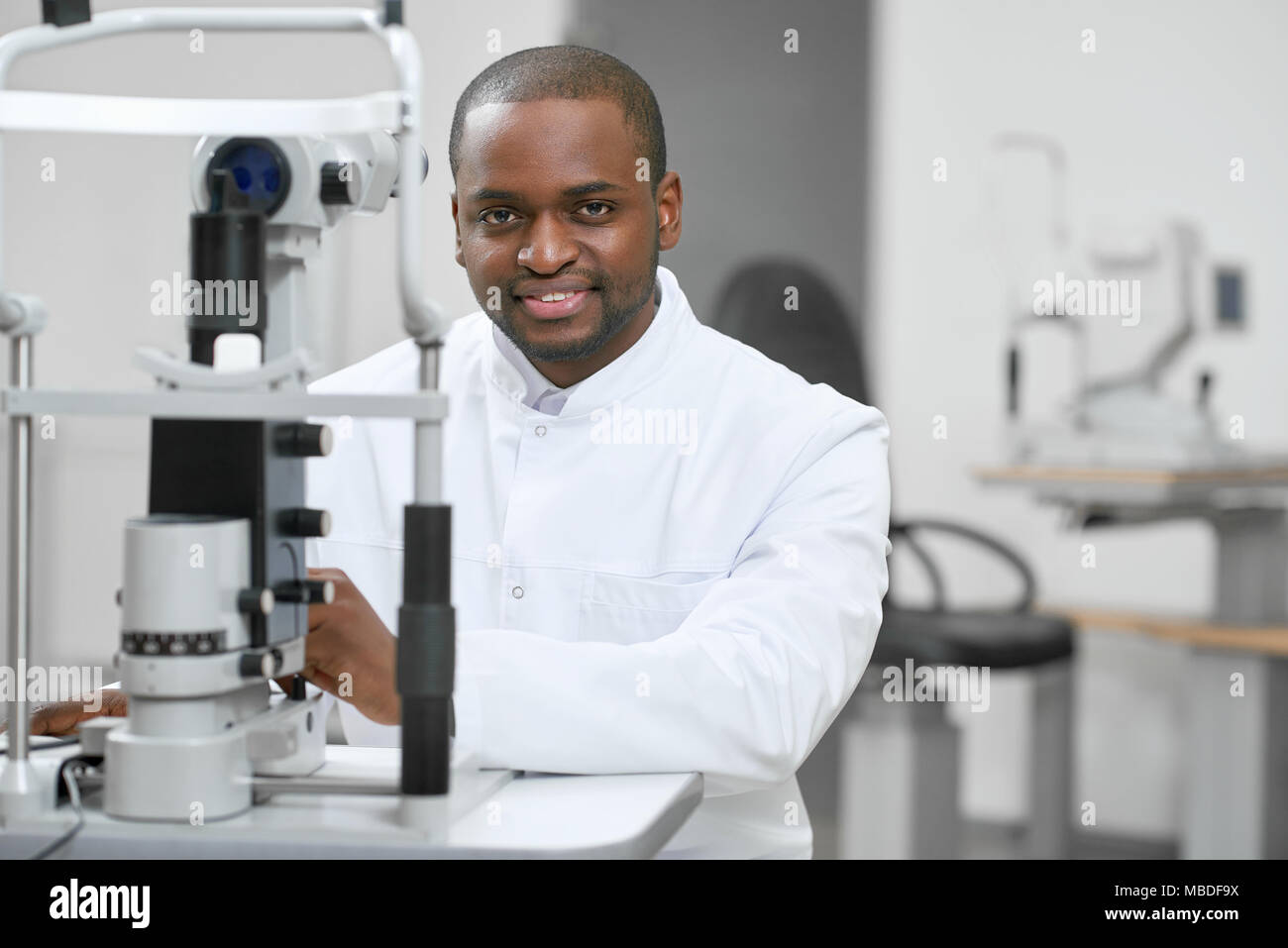 Giovane uomo in piedi in prossimità di apparecchiature mediche per la visione di controllo e di miglioramento. Cerca gentile e pronto per la terapia. Indossando classico bianco shirt. Foto Stock