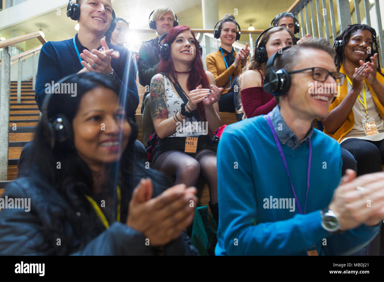 Udienza sorridente con cuffie battendo le mani a una conferenza Foto Stock