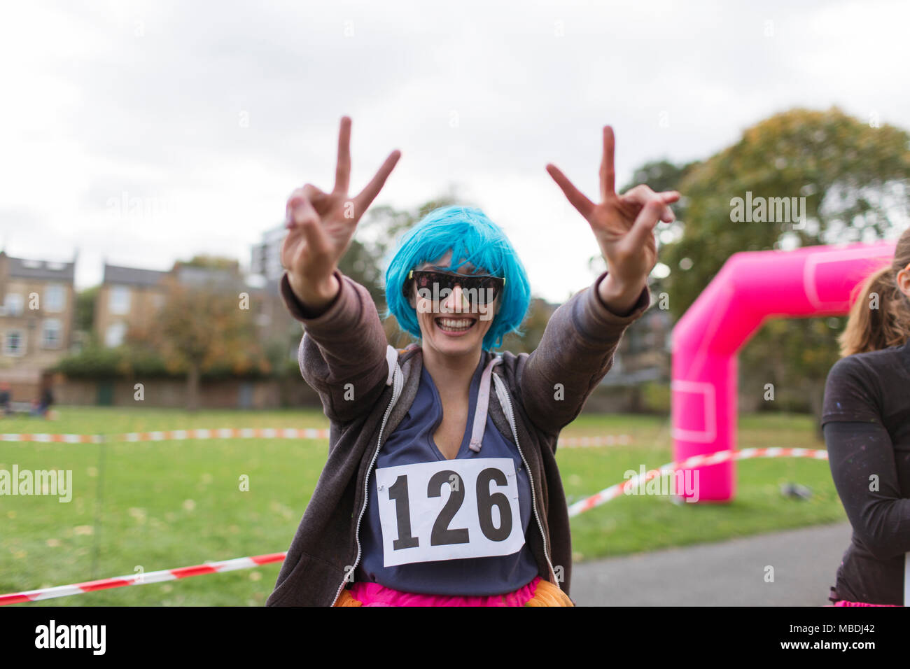 Ritratto femminile entusiasta runner in parrucca gesti segno di pace alla carità eseguire in posizione di parcheggio Foto Stock