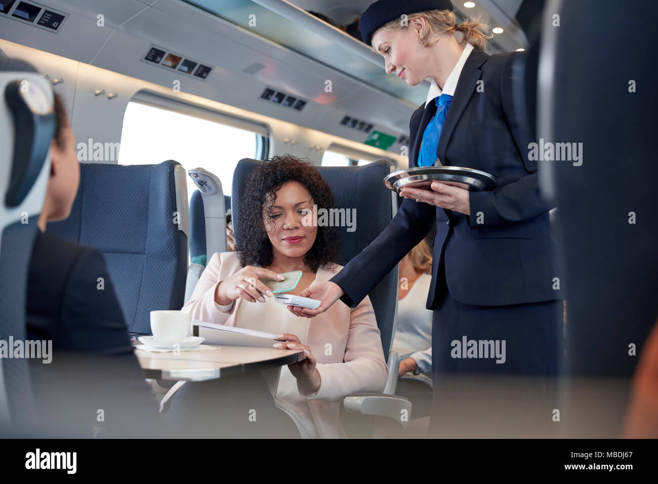 Imprenditrice con smart phone utilizzando il pagamento senza contatto, prestando attendant sul treno passeggeri Foto Stock