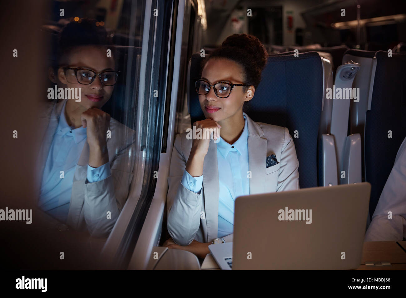 Fiducioso, riflessivo imprenditrice guardando fuori della finestra sul treno passeggeri di notte, lavorando al computer portatile Foto Stock