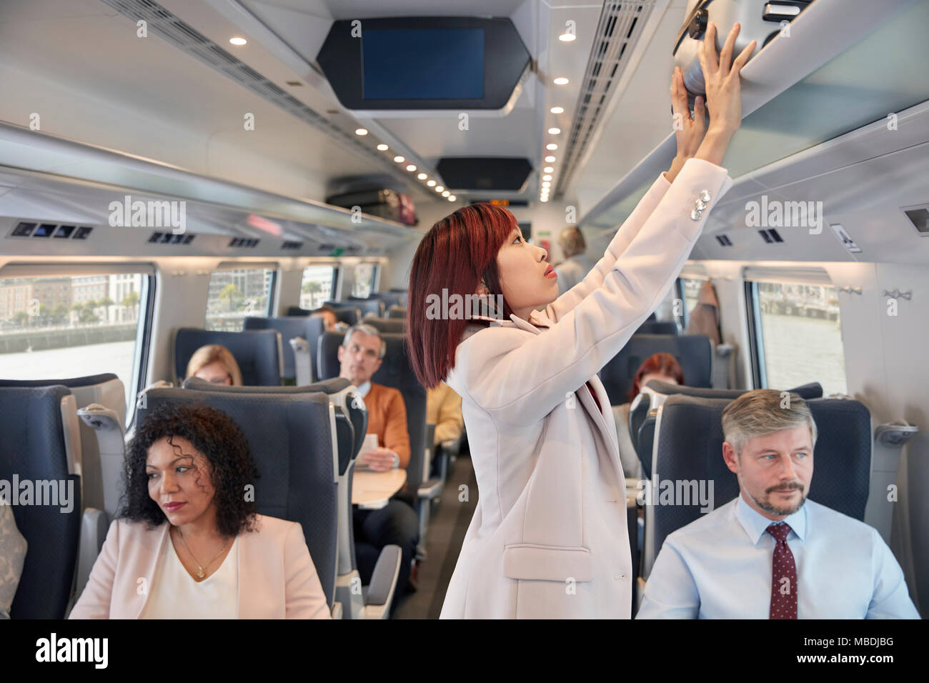 Imprenditrice di stivaggio valigia nel vano di overhead sul treno passeggeri Foto Stock