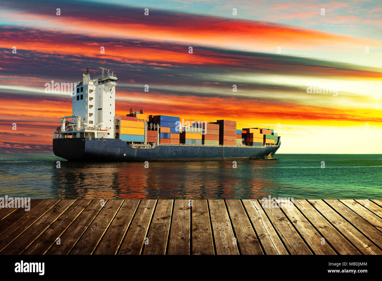 Vista dal molo in legno con contenitore nave sul mare durante il tramonto. Foto Stock