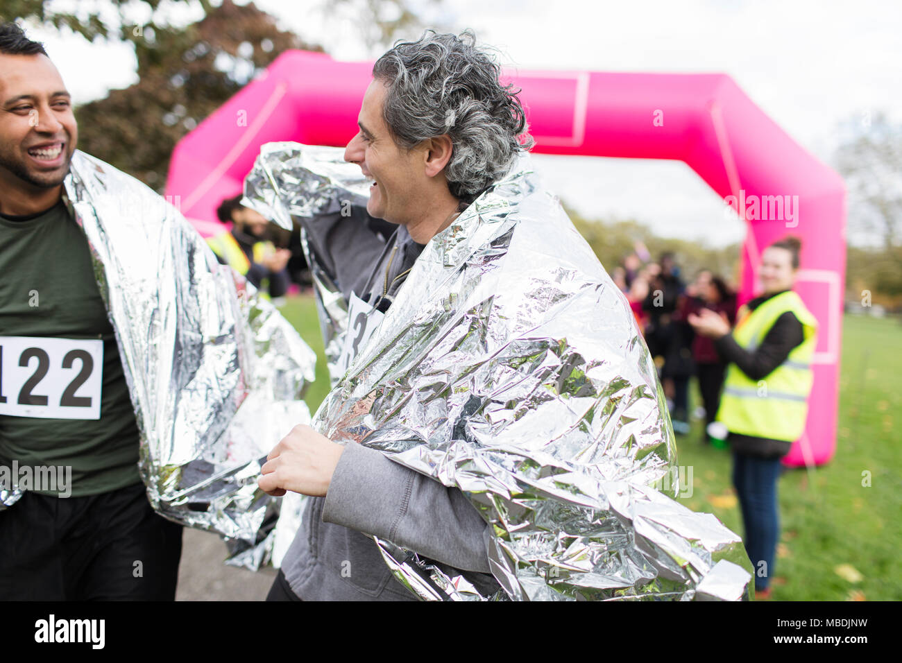 Maschio sorridente maratoneti terminando gara, indossando coperte termiche Foto Stock