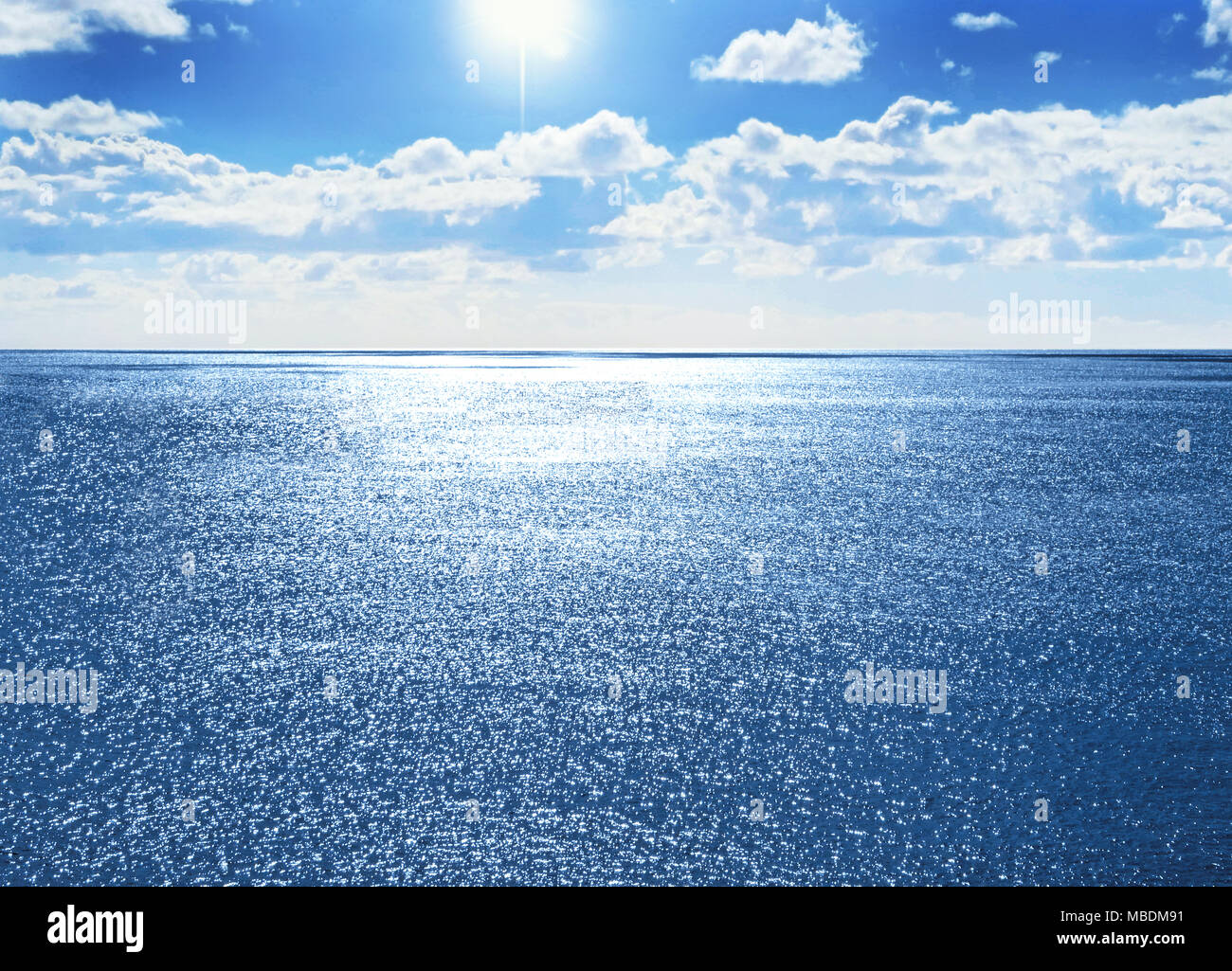 Un mare scintillante o seascape sfondo con acqua scintillante e cielo blu con nuvole soffici e copia di spazio. Foto Stock