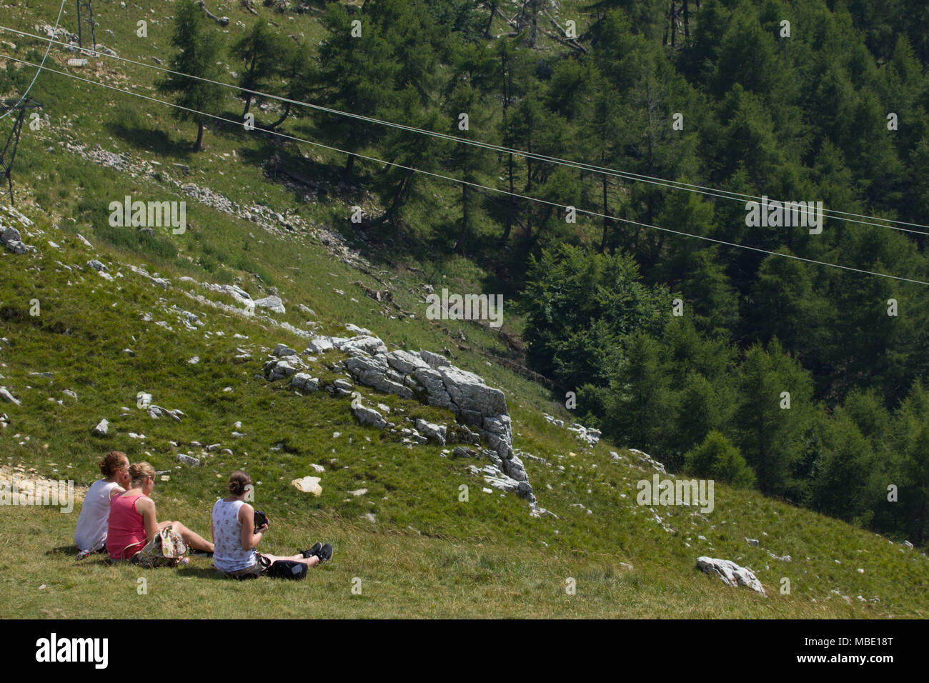 Tre amici seduti ammirando la vista dal Monte Baldo, uno scattare una fotografia, Italia Foto Stock