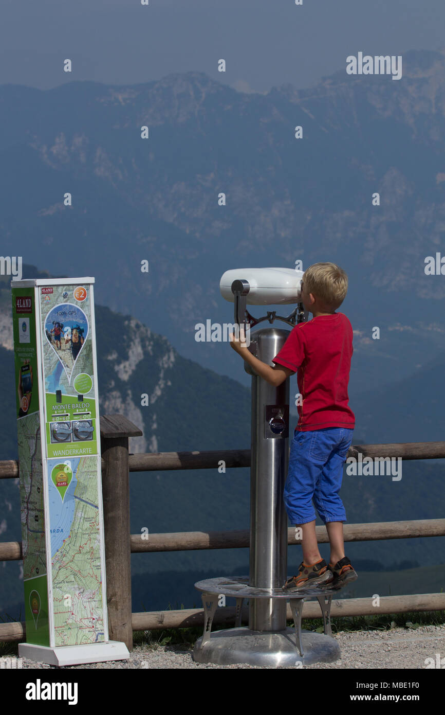 Un bambino curioso cerca su una catena montuosa sulla sommità del Monte Baldo vicino alla stazione della funivia, Italia Foto Stock