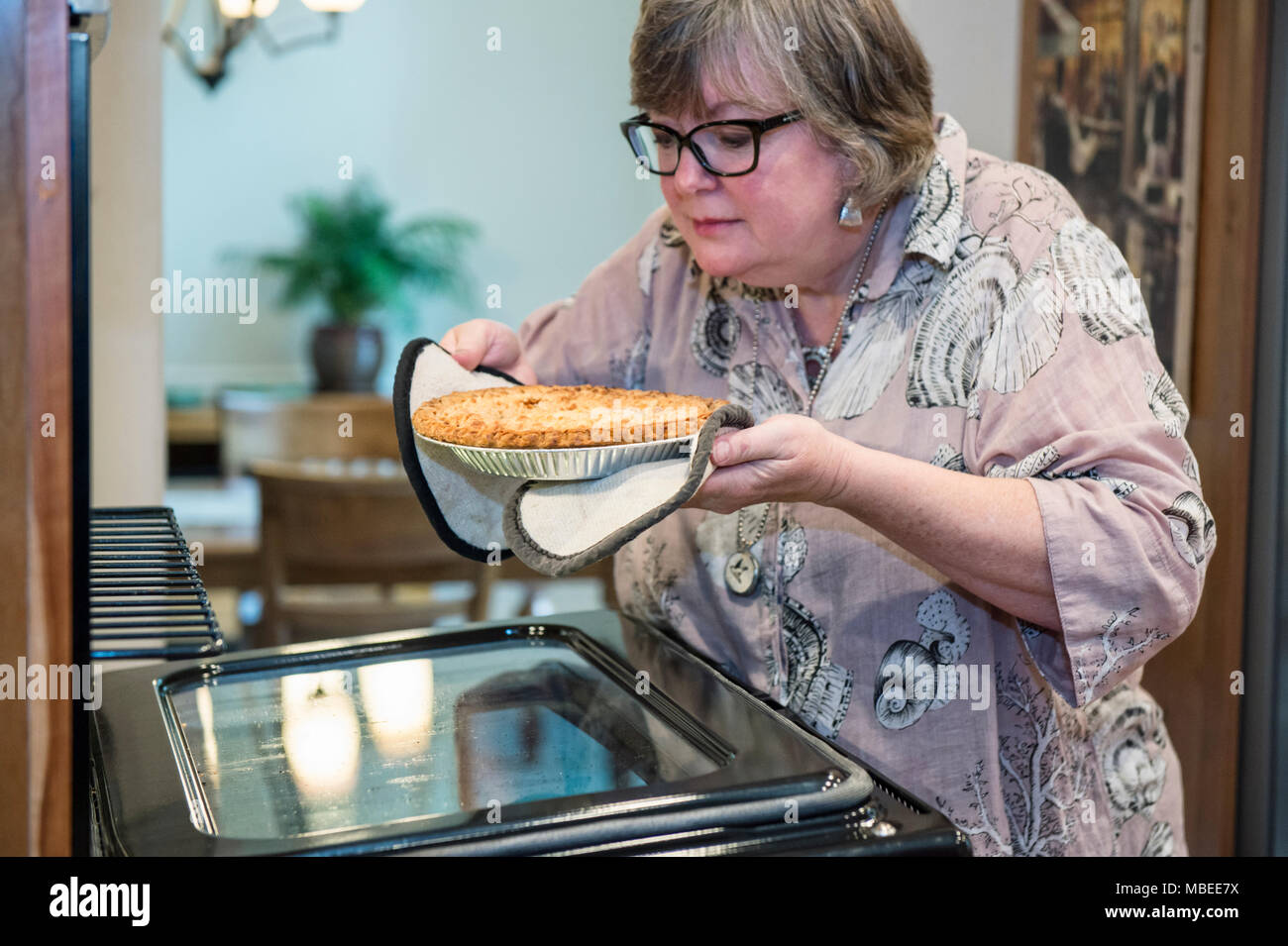 Donna senior di controllo a vedere se una casa torta cotto è pronto a venire fuori dal forno. Foto Stock