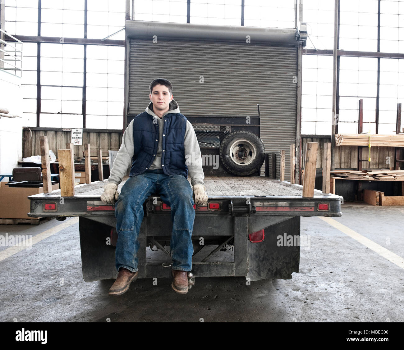 Un giovane caucasico operaio di fabbrica seduta sul dorso di un automezzo a pianale in lamiera di fabbrica. Foto Stock