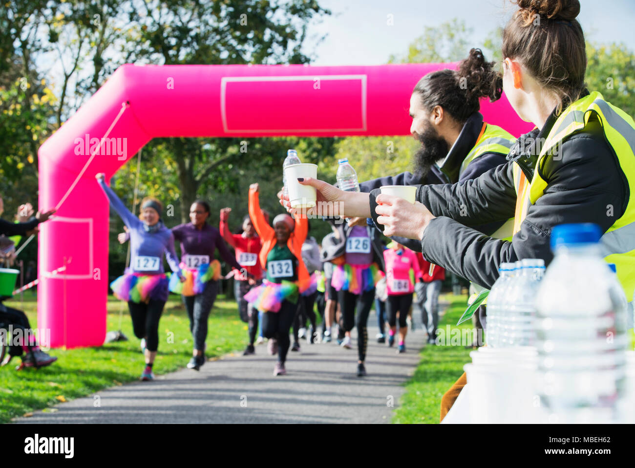 Volontari con acqua pronto per eseguire la carità corridori Attraversamento linea di finitura Foto Stock