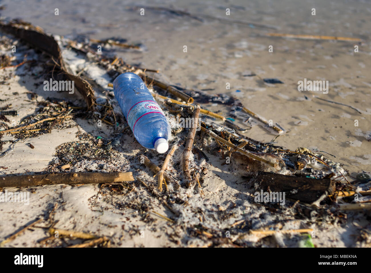 La bottiglia di plastica rifiuti giace lavato fino sulla riva di una spiaggia di sabbia bianca Foto Stock