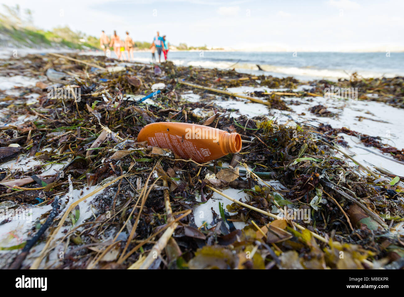 Rifiuti di plastica si trova lavato fino sulla riva di una spiaggia di sabbia bianca con gente che cammina in background Foto Stock