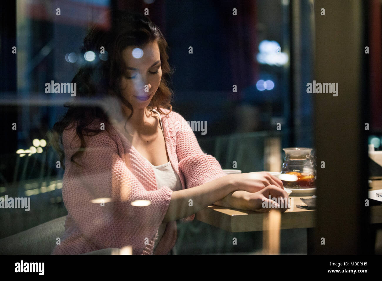 Giovane seduto da una finestra al caffè locali luogo e godendo di notte invernale con bevande calde e conversazione informale. Scattato dall'esterno attraverso il vento Foto Stock