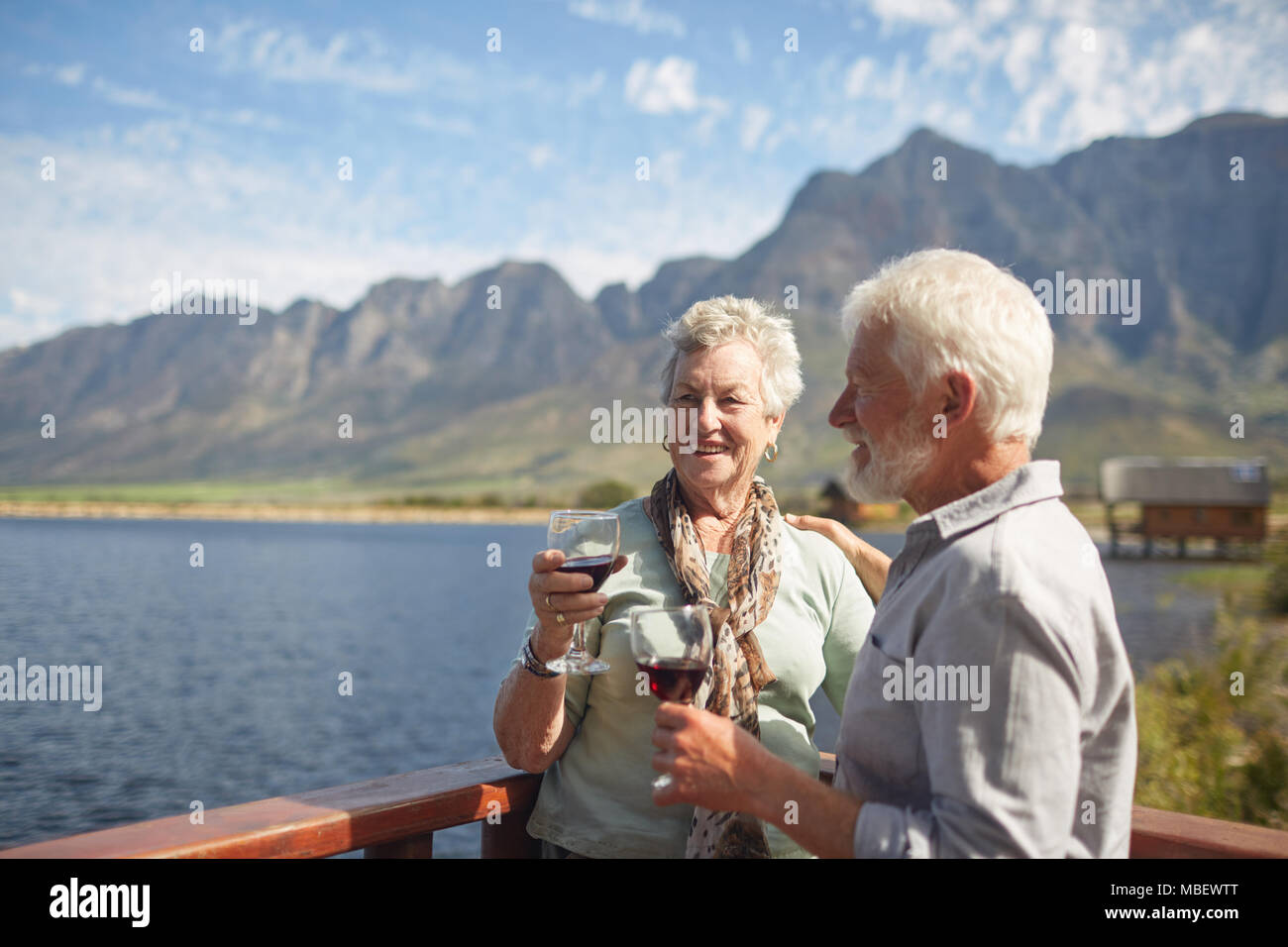 Attiva sorridente coppia senior di bere vino rosso su estivo soleggiato balcone sul lago Foto Stock