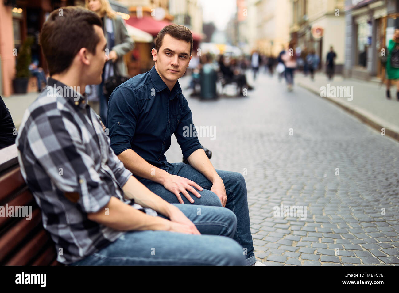 Due uomini di sedersi sulla panchina e talk su strada Foto Stock