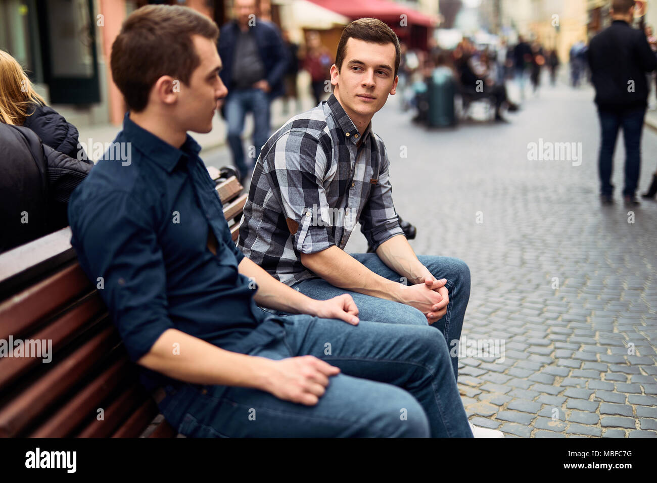 Due uomini di sedersi sulla panchina e talk su strada Foto Stock