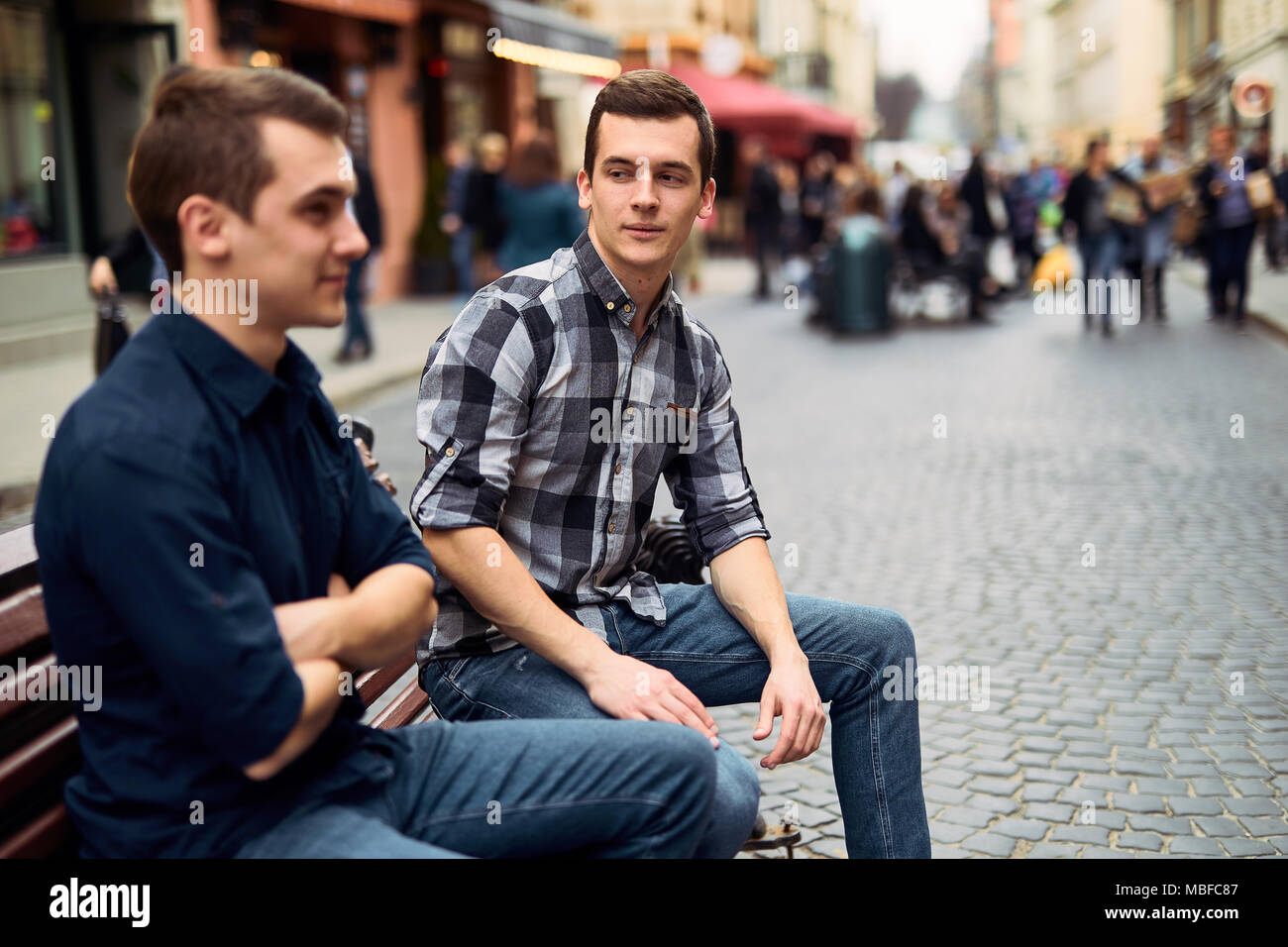 Due uomini di sedersi sulla panchina e talk su strada Foto Stock