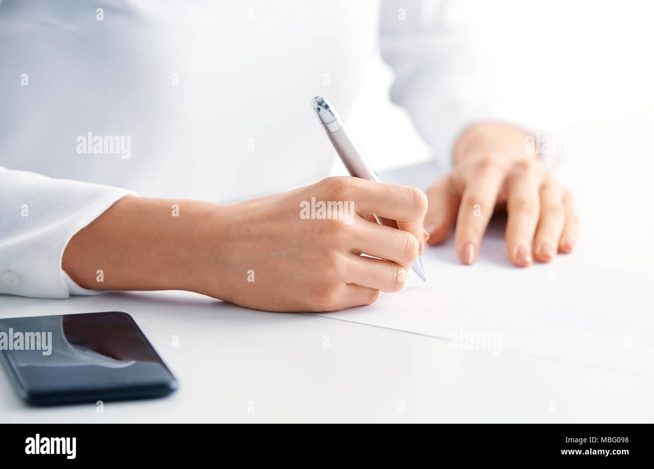 Close-up shot di imprenditrice la mano che tiene la penna e a scrivere qualcosa per il PC portatile mentre è seduto alla scrivania in ufficio. Foto Stock
