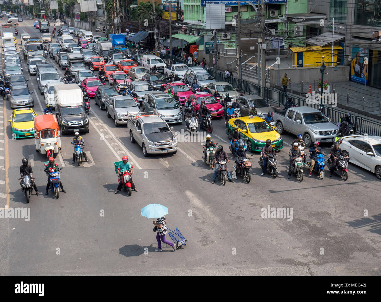 Una donna zona pedonale con un ombrello attraversa una strada trafficata di fronte al traffico pesante in coda su un nodo stradale in Bangkok city street in Thailandia Foto Stock