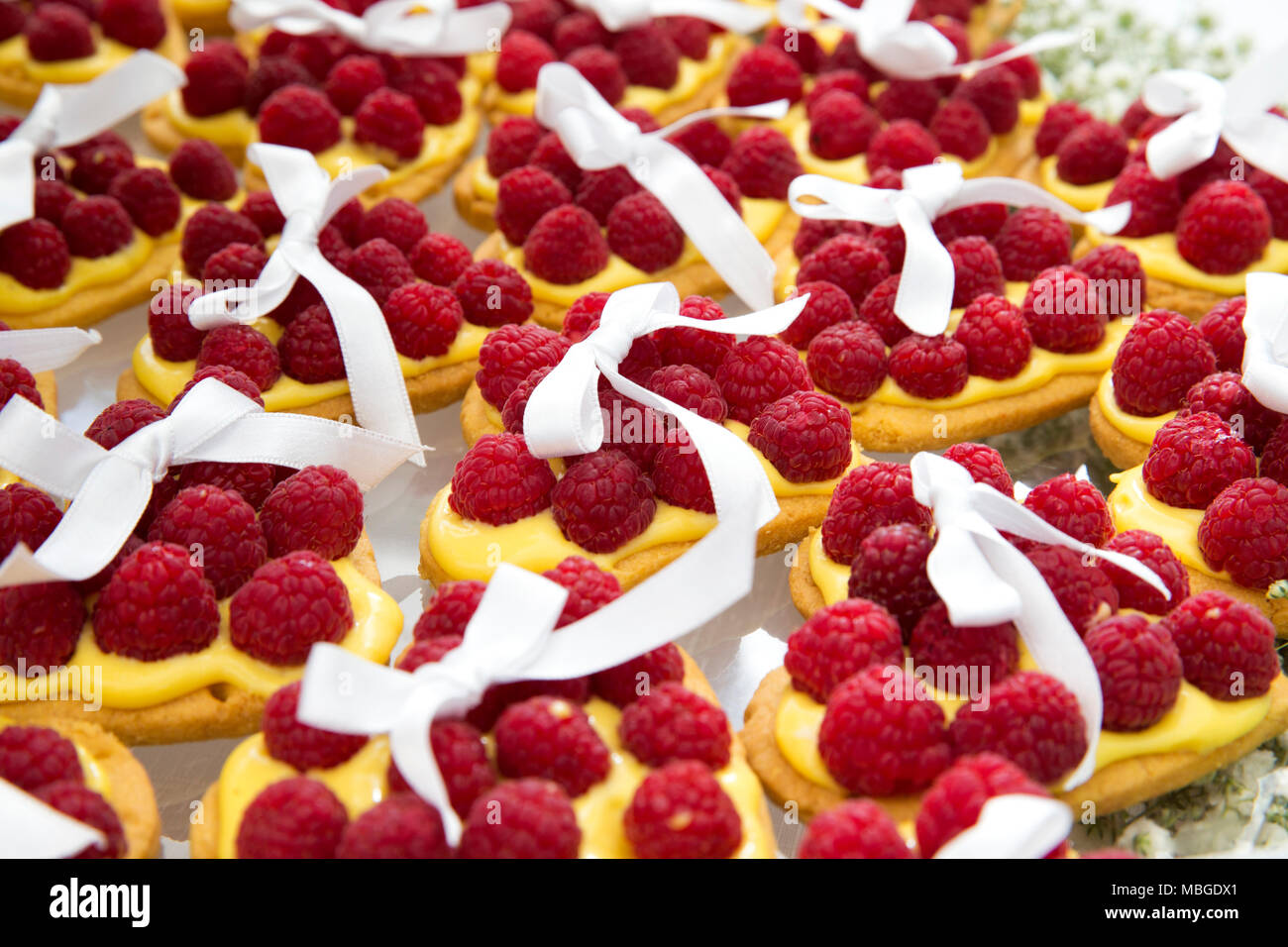 Primo piano di una torta di nozze composto da numerose piccole torte a forma di cuore con crema pasticcera e lampone. Decorata con un nastro bianco su ogni torta Foto Stock