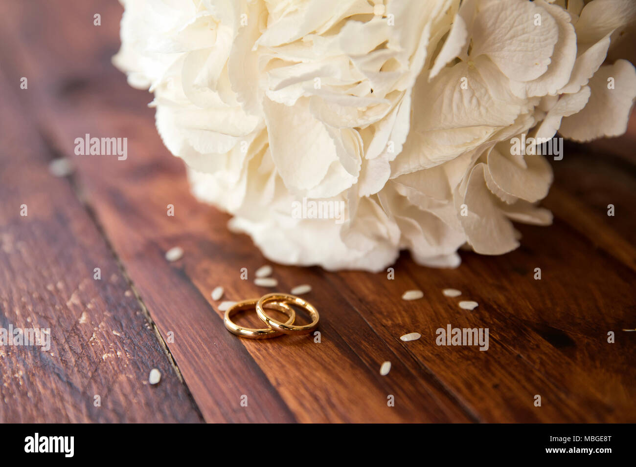 Inquadratura orizzontale di un bouquet nuziale con gli anelli di nozze con i chicchi di riso sul tavolo un bouquet nuziale e anelli d oro sono al buio su un tavolo di legno Foto Stock