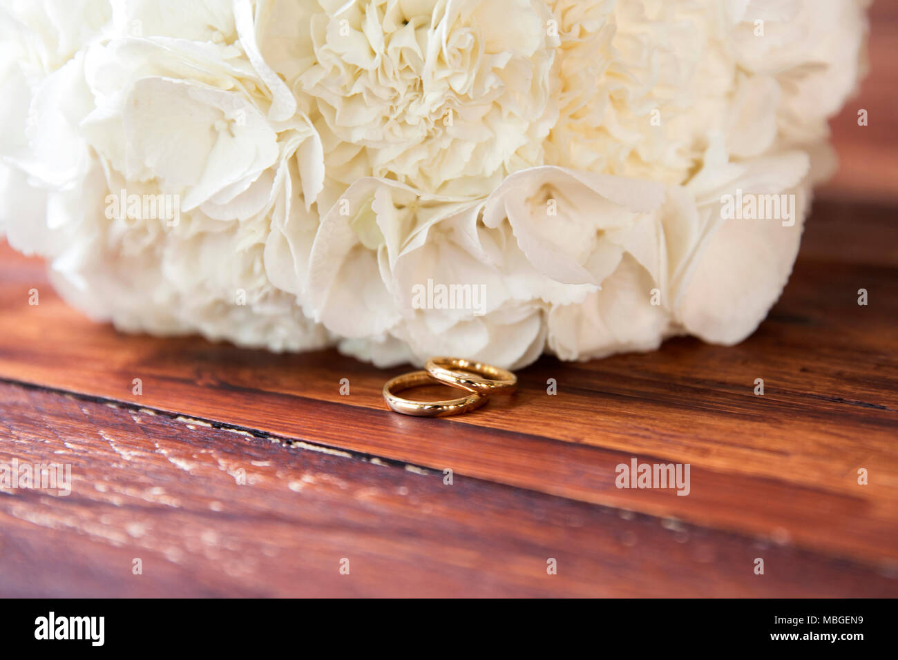 Un primo piano di due anelli d oro nella parte anteriore del bouquet della sposa su una tavola di legno Foto Stock