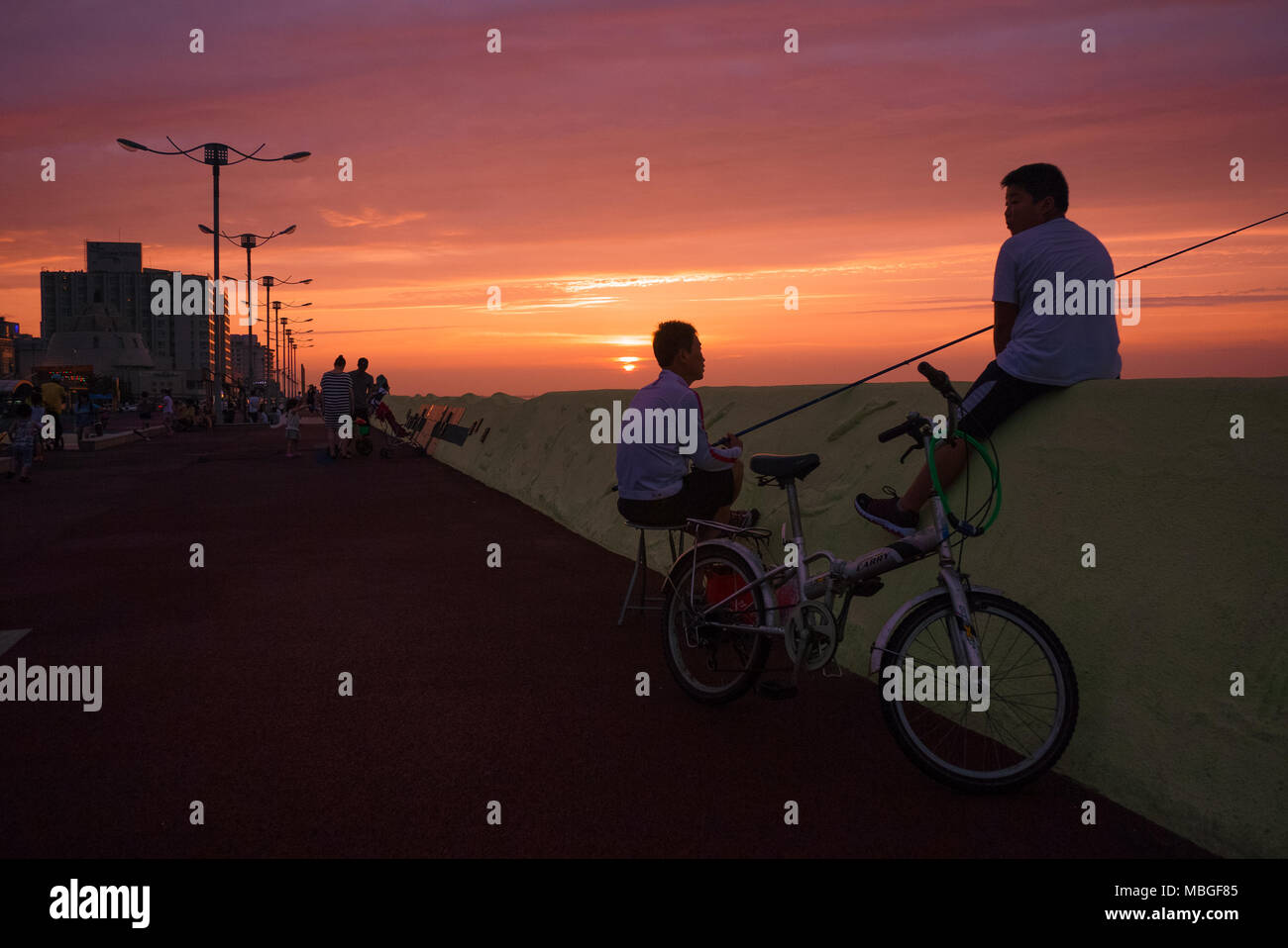 Un padre e figlio seduti a seawall e pesce al tramonto nella città di Jeju, Jeju Island, la Corea del Sud. Foto Stock